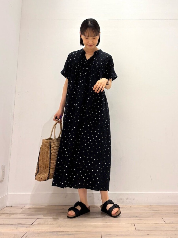 ドット柄黒ワンピースの女性が、かごバッグを持ち下を向いて微笑む ドット柄黒ワンピースの女性が、かごバッグを持ち下を向いて微笑む