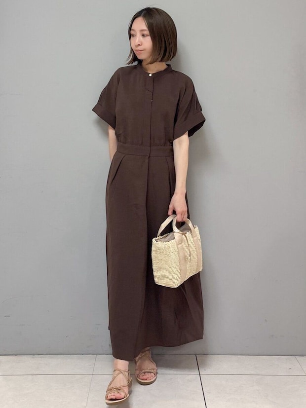 ダークブラウンのシャツワンピースを着た女性が、かごバッグを持ち横を向く