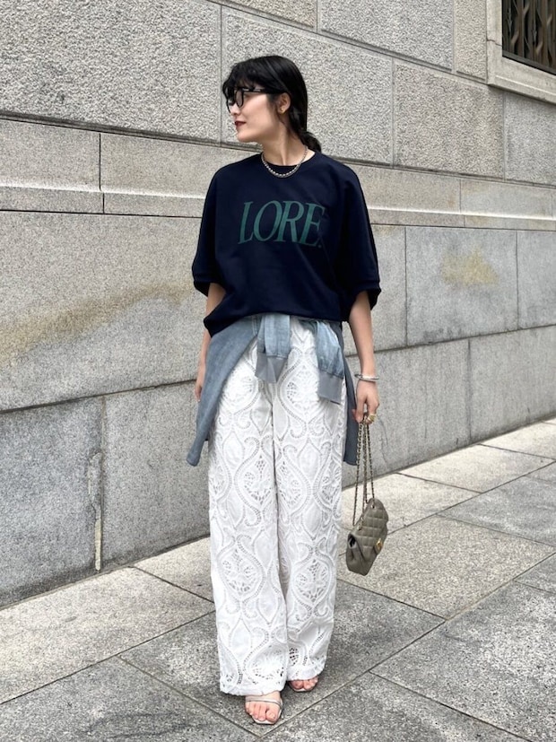 ネイビーのロゴTシャツと白いレースパンツを着用し、腰にシャツを巻いた女性 ネイビーのロゴTシャツと白いレースパンツを着用し、腰にシャツを巻いた女性