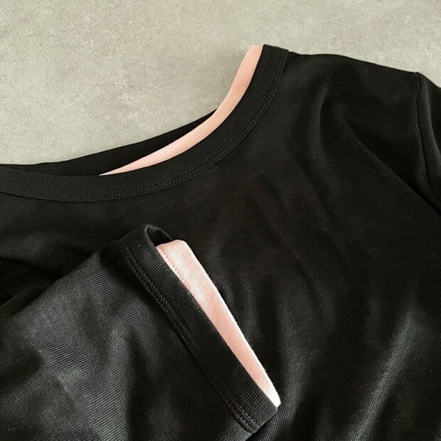 黒いTシャツの襟元と袖口のアップ。袖からピンクの生地が見える。