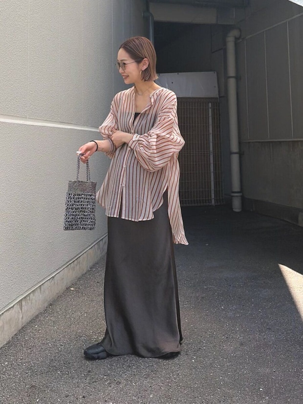 シアーストライプシャツとグレーサテンスカートを着用し、屋外に立つ女性