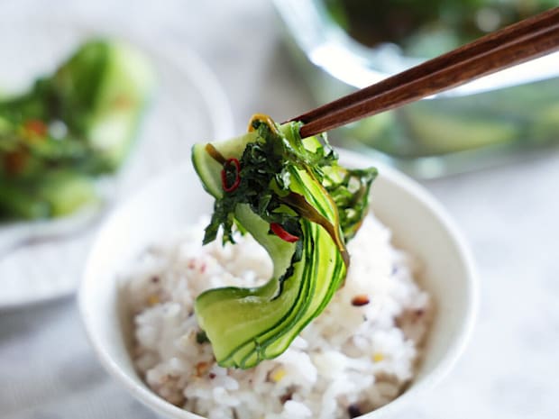 箸でひらひらきゅうりの浅漬けを掴み、白いご飯が盛られたお茶碗の上に乗せようとしている
