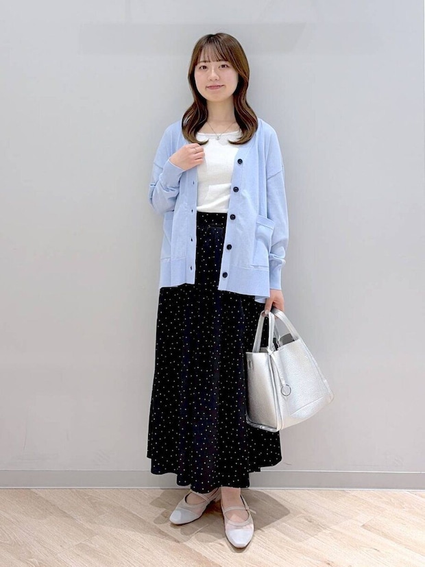 水色の長袖カーディガンとドット柄ロングスカートの女性が立っている 水色の長袖カーディガンとドット柄ロングスカートの女性が立っている