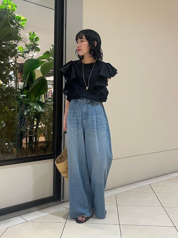 黒のフリルブラウスとワイドデニムを着用