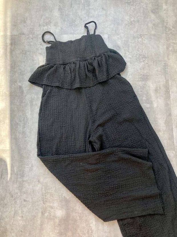 黒いペプラムクロスシャーリングオールインワンが床に広げられている 黒いペプラムクロスシャーリングオールインワンが床に広げられている