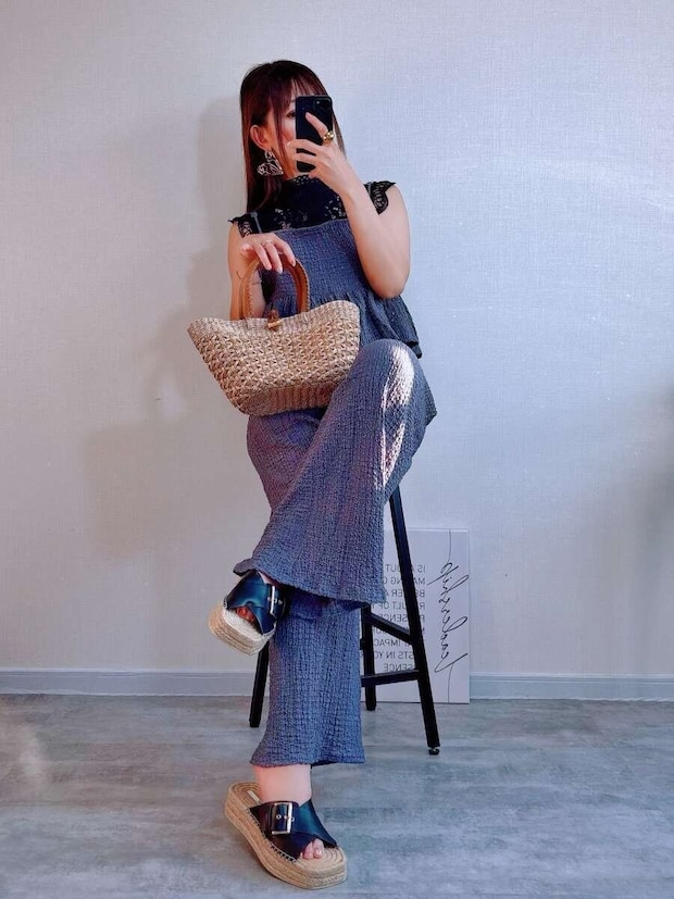 黒レースブラウスを着用した女性がグレーのオールインワンを着て椅子に座りかごバッグを持っている 黒レースブラウスを着用した女性がグレーのオールインワンを着て椅子に座りかごバッグを持っている