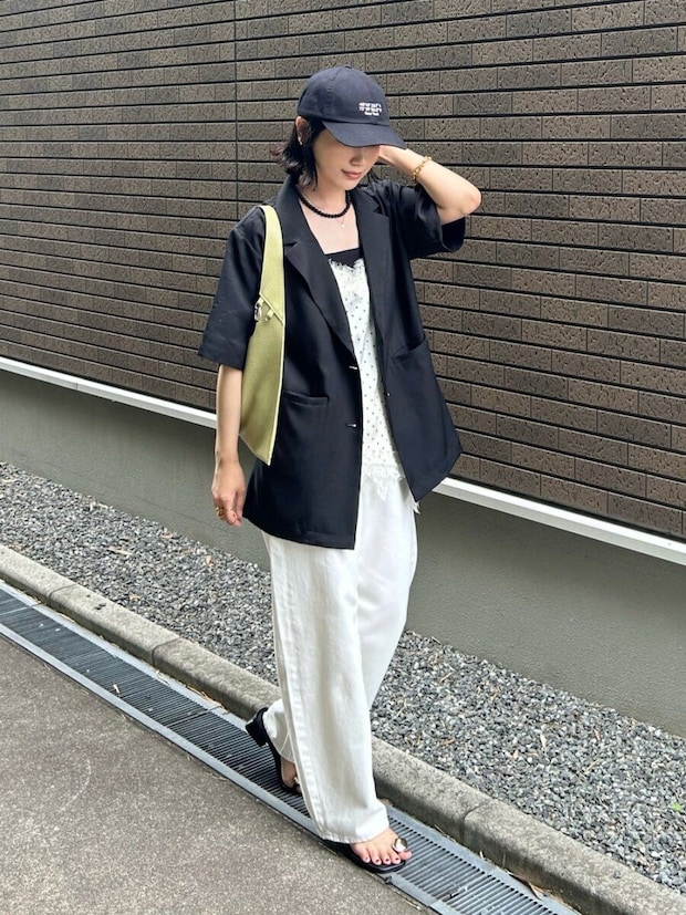 黒の半袖ジャケットと白ワイドパンツ、キャップを被った女性が歩いている。 黒の半袖ジャケットと白ワイドパンツ、キャップを被った女性が歩いている。