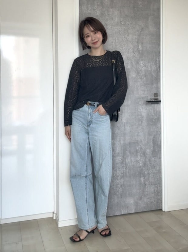 黒いレースブラウスとデニムのパンツスタイルで立つ女性