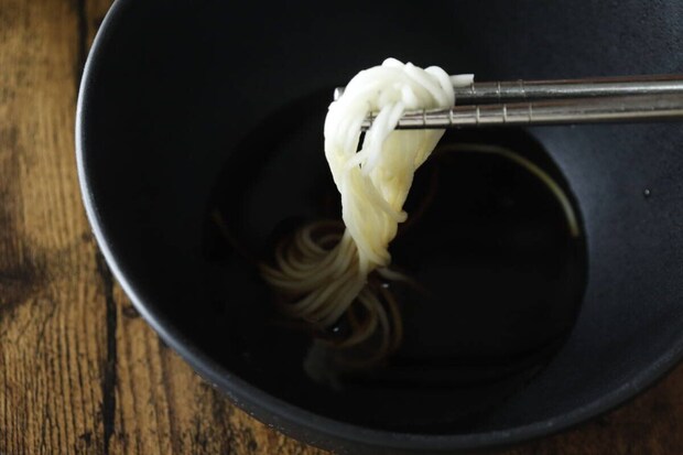 黒い器のめんつゆに、箸でそうめんを浸している手元