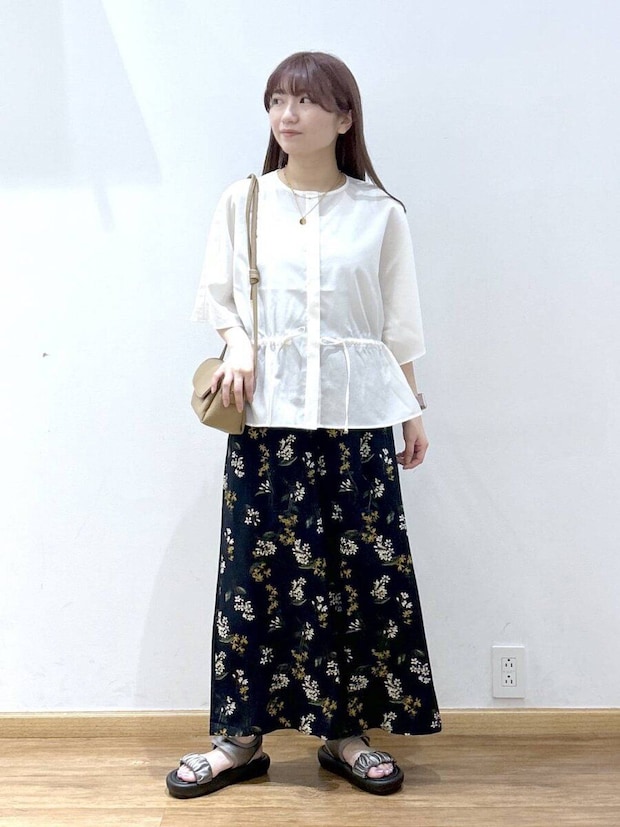 白のドローストリングブラウスと花柄ロングスカートを着た女性