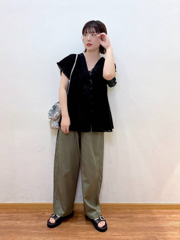 黒のギャザーブラウスとカーキワイドパンツを着てメガネに手を添える女性