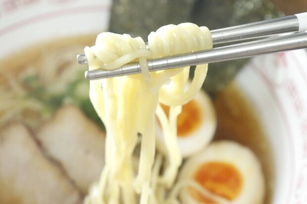 箸で持ち上げられたラーメンの麺のアップ。奥にはチャーシューと煮卵