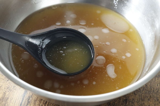 銀色のボウルに入ったラーメンスープの素を黒いお玉ですくっている様子