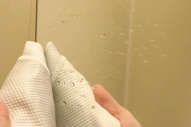 水滴のついた鏡を白いクロスで拭いている手元