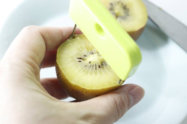 半分に切ったキウイに緑色の皮むき器を差し込んでいる手元 半分に切ったキウイに緑色の皮むき器を差し込んでいる手元