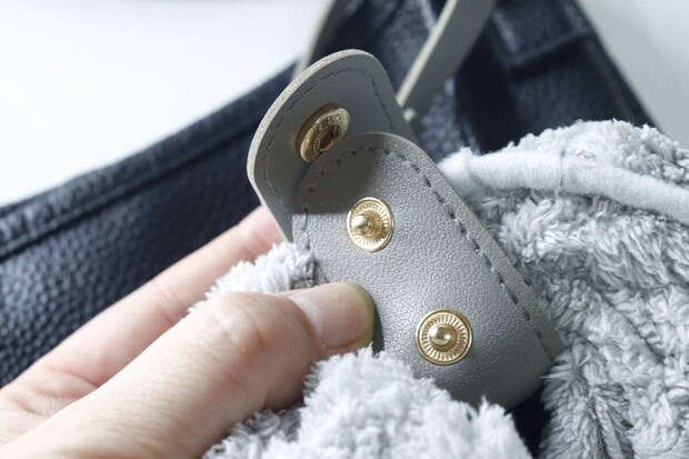 タオルホルダーのスナップボタンでグレーのタオルを固定する手元