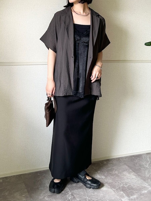 黒いロングスカートに黒いサテンキャミソールと茶色の半袖ジャケットを重ね着した女性の全身
