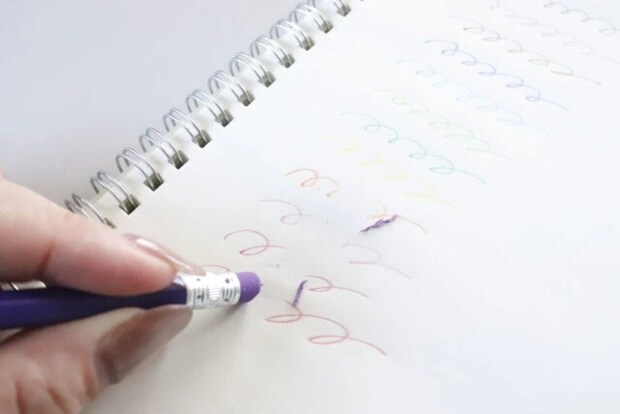 消せる色鉛筆の消しゴムでノートの線を消している手元