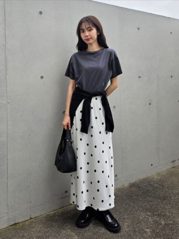 グレーTとドット柄スカート、カーデ腰巻きの女性がバッグを持ち立つ
