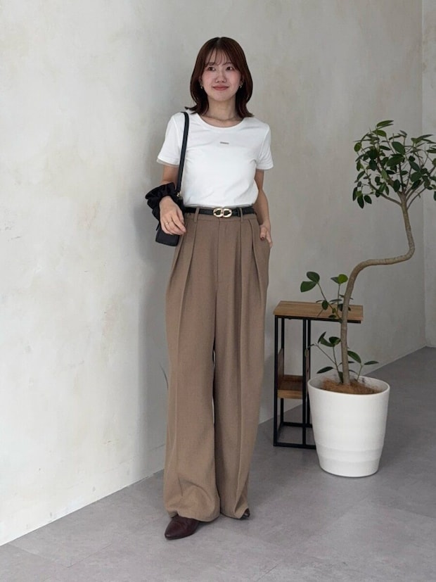 白Tシャツとブラウンワイドスラックス姿で立つ女性