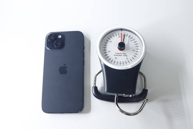 黒いスマートフォンと並べて置かれたスーツケース用計り。計りの方が大きい。