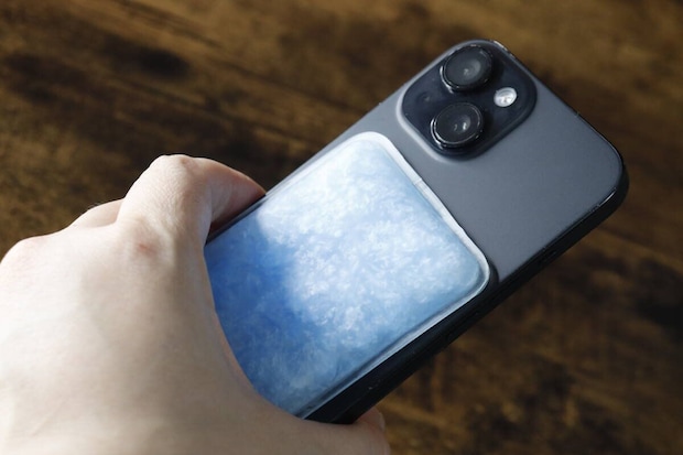スマートフォンの背面に青い冷却パッドを貼り付けている様子