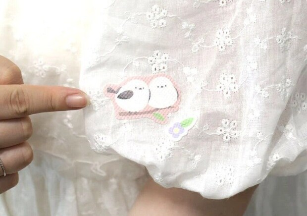 女性が白いブラウスの袖にシマエナガ柄の虫よけシールを貼って指差している 女性が白いブラウスの袖にシマエナガ柄の虫よけシールを貼って指差している