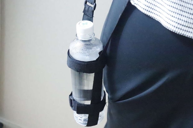 女性がボトルホルダーを肩から下げてペットボトルを携帯している 女性がボトルホルダーを肩から下げてペットボトルを携帯している