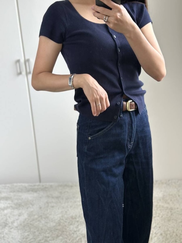 ネイビーのカーディガンとワイドデニムを着用した女性がスマホを構える