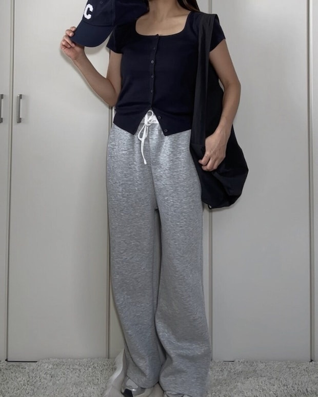 ネイビーのカーディガンとグレーのスウェットパンツ、キャップを持った女性 ネイビーのカーディガンとグレーのスウェットパンツ、キャップを持った女性
