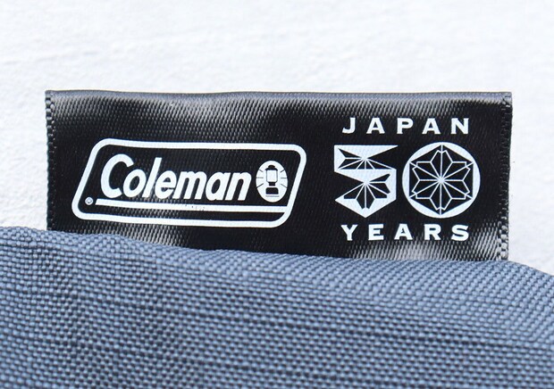 トートバッグに縫い付けられた「Coleman JAPAN 50 YEARS」の黒いタグのクローズアップ。 トートバッグに縫い付けられた「Coleman JAPAN 50 YEARS」の黒いタグのクローズアップ。