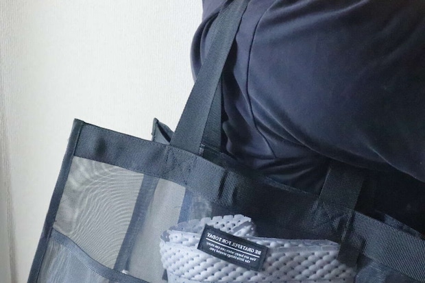 黒いメッシュバッグを肩に掛けている人の上半身、バッグの中身が少し見える 黒いメッシュバッグを肩に掛けている人の上半身、バッグの中身が少し見える