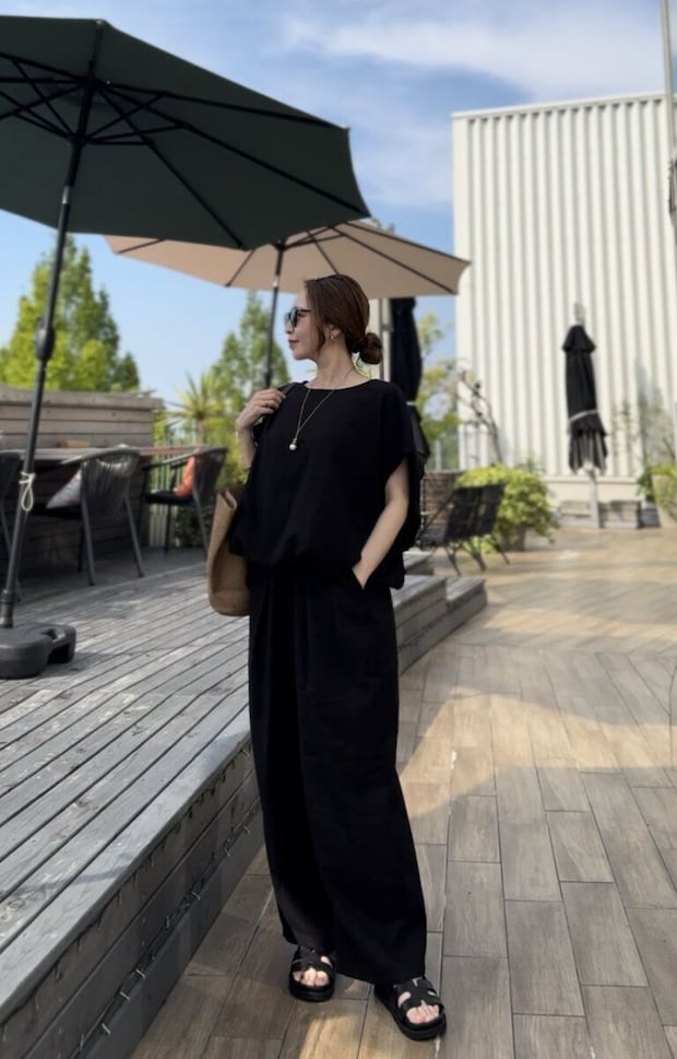 黒いリネンセットアップの女性が屋外テラスで横向きに立つ 黒いリネンセットアップの女性が屋外テラスで横向きに立つ
