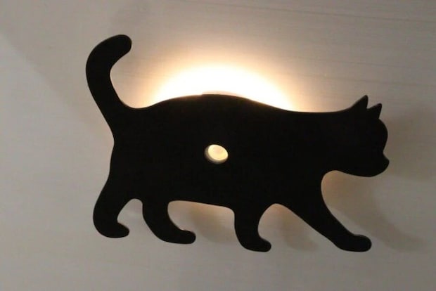 壁に設置された黒い猫のシルエットプレートの裏から光が漏れている様子