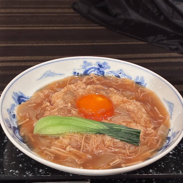 卵黄と青菜が乗ったあんかけ料理が盛り付けられた白い器