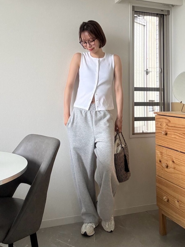 白いノースリーブとスウェットパンツの女性が、壁に寄りかかり笑顔で立つ 白いノースリーブとスウェットパンツの女性が、壁に寄りかかり笑顔で立つ