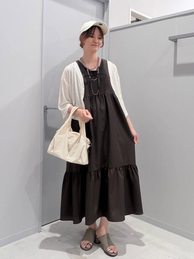 白いカーディガンと黒ワンピースの女性がバッグを持ち笑顔