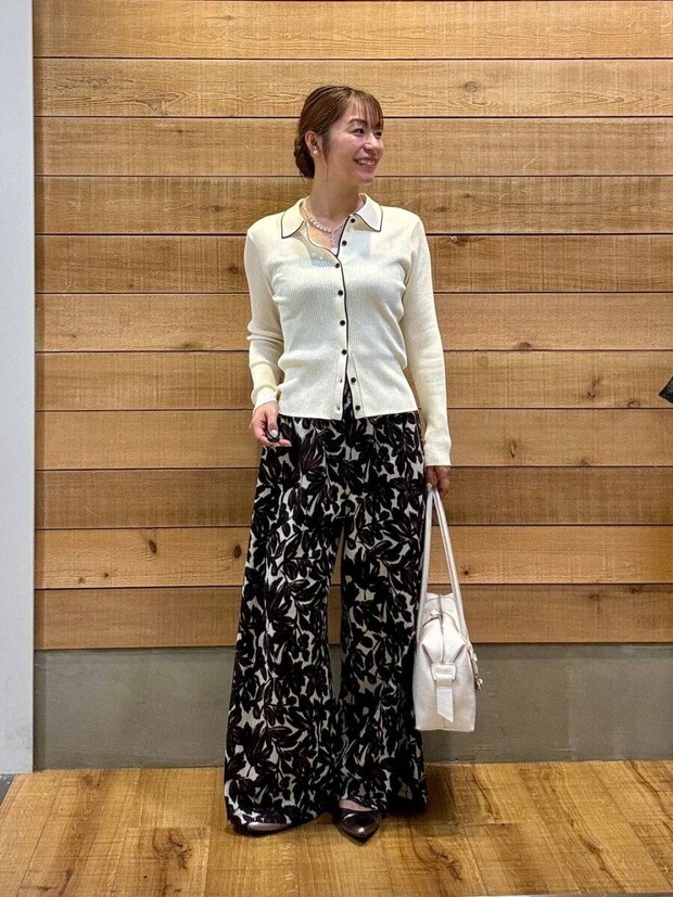 白い襟付きカーディガンと柄パンツの女性が笑顔で立つ 白い襟付きカーディガンと柄パンツの女性が笑顔で立つ