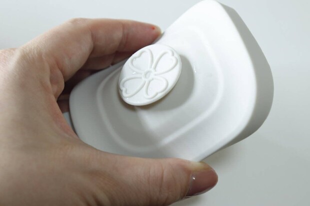 女性が白い保存容器の蓋にある桜の花のようなエア弁を押している 女性が白い保存容器の蓋にある桜の花のようなエア弁を押している