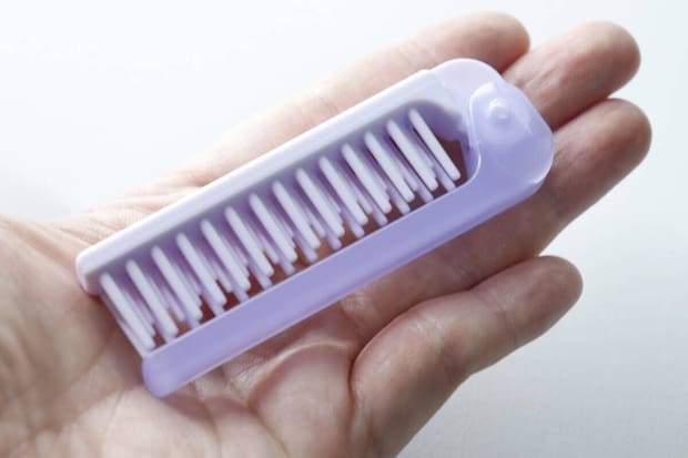 手のひらに乗せられた紫色の折りたたみ式ヘアブラシ 手のひらに乗せられた紫色の折りたたみ式ヘアブラシ