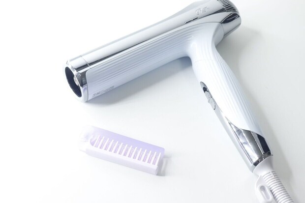 白いドライヤーの横に置かれた紫色の折りたたみヘアブラシ
