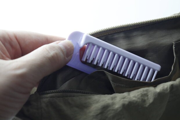 カバンのポケットに紫色の折りたたみヘアブラシを入れる手