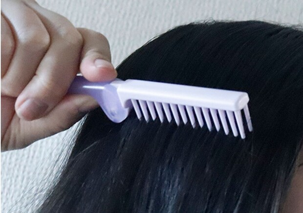 女性が黒い髪を紫色の折りたたみヘアブラシでとかしている