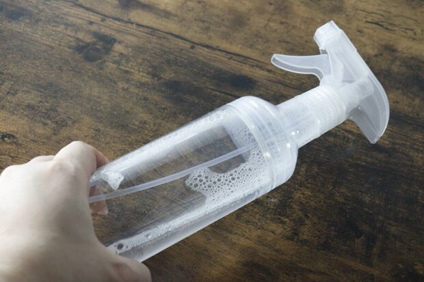 液体が入った透明なスプレー容器を片手で持っている 液体が入った透明なスプレー容器を片手で持っている