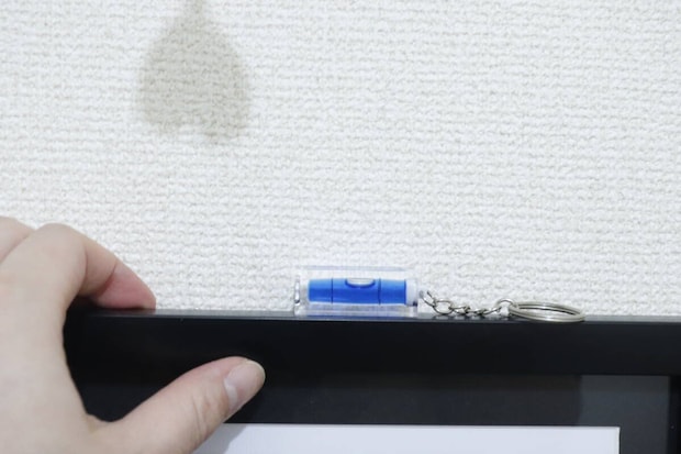 額縁の縁に置かれたキーホルダー水平器と手を添えている 額縁の縁に置かれたキーホルダー水平器と手を添えている