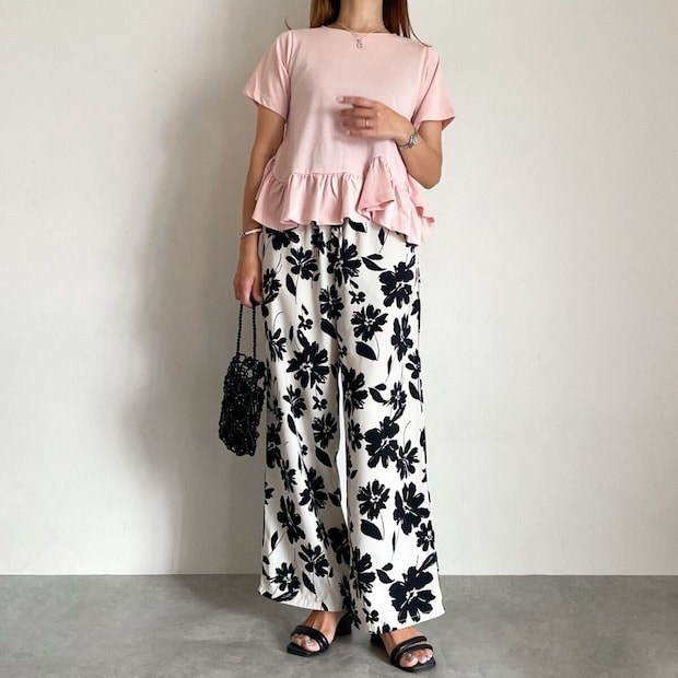 ピンクのペプラムトップスと花柄ワイドパンツ、黒いバッグの大人コーデ。 ピンクのペプラムトップスと花柄ワイドパンツ、黒いバッグの大人コーデ。