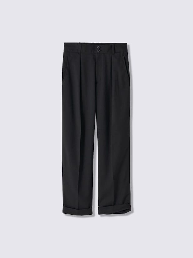 黒いタック入りのテーパードパンツ、裾はロールアップされている 黒いタック入りのテーパードパンツ、裾はロールアップされている