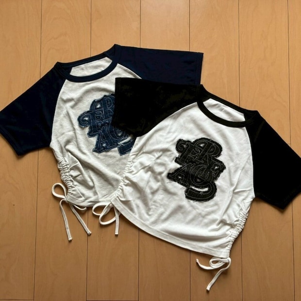 黒と白のラグランTシャツが木床に並べられ裾にリボンが見える 黒と白のラグランTシャツが木床に並べられ裾にリボンが見える
