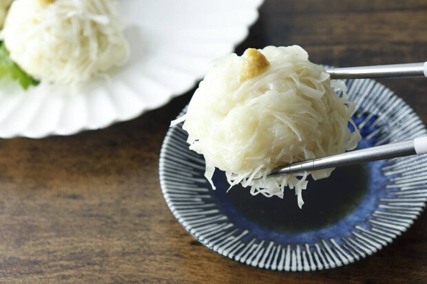 青釉たれ皿に盛り付けられた焼売を箸でつまんでいる