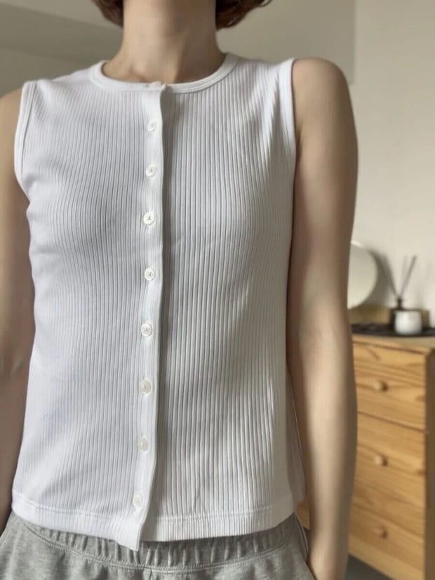 白いリブ素材のフロントボタンノースリーブトップスを着用した女性の胸元アップ 白いリブ素材のフロントボタンノースリーブトップスを着用した女性の胸元アップ
